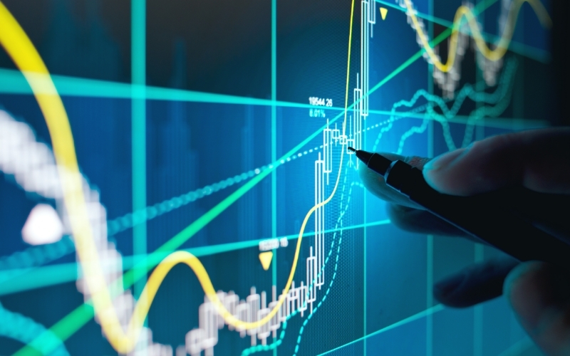 hand holding a pin tapping a touch screen with a market candle stick chart