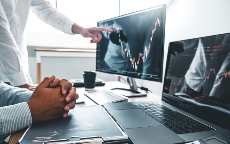 man at desk pointing at stock chart onscreen