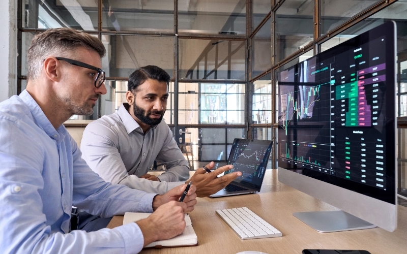 two men sitting at a desk looking over portfolio charts